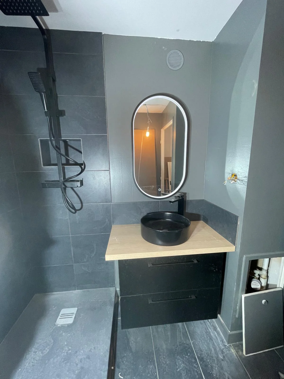 Salle de bain contemporaine réalisée par EMS TRAVAUX — carrelage gris anthracite, miroir ovale et vasque noire
